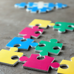 Ordentlich aufgereihte Puzzleteile in Primärfarben auf grauem Grund | Heilpädagogische Förderung Hof Wiesengrund